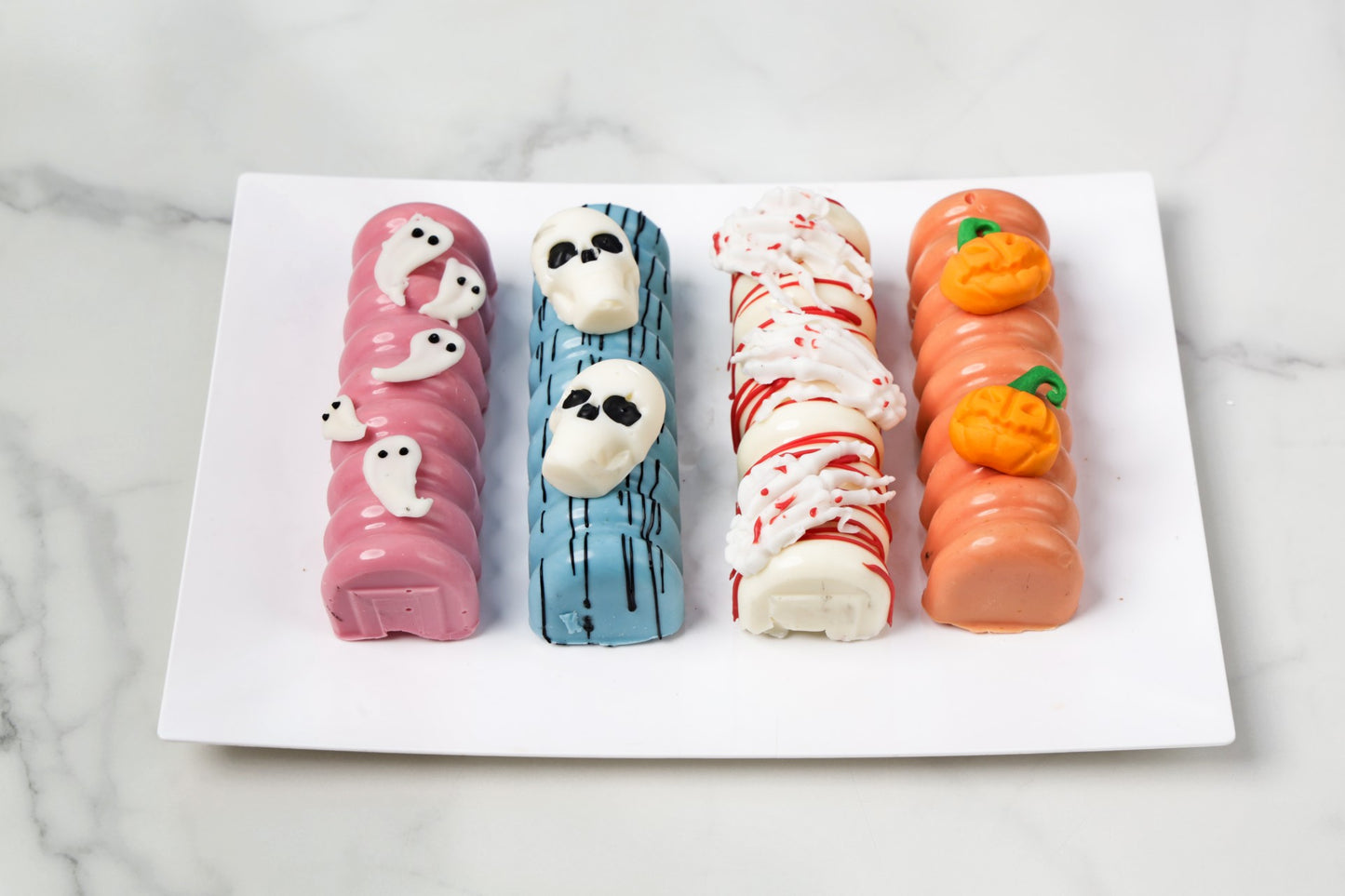 Four Halloween-themed hot dogs on a white plate with a marble background