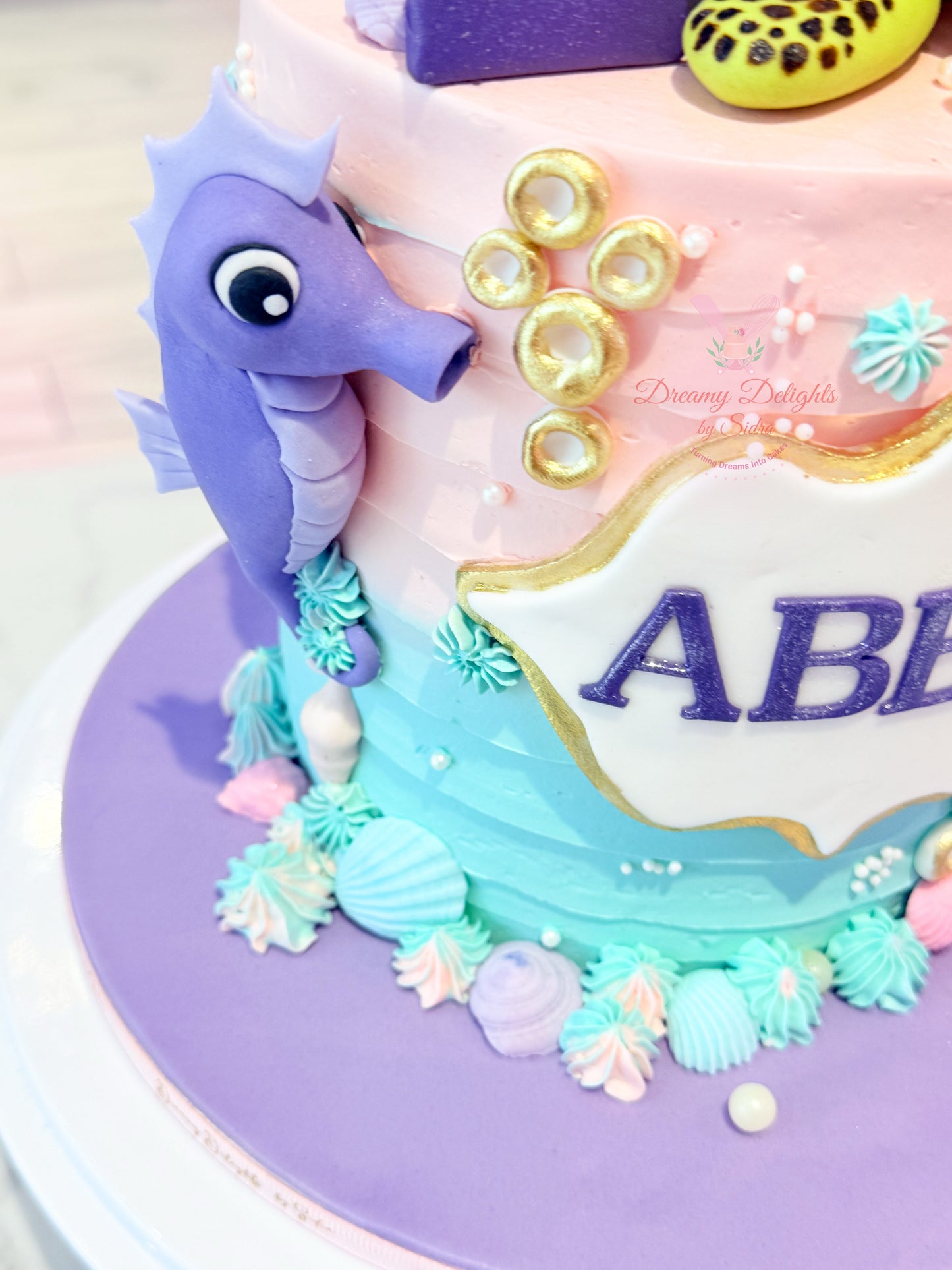 Decorative cake with a purple seahorse figure and 'ABE' text on a colorful background