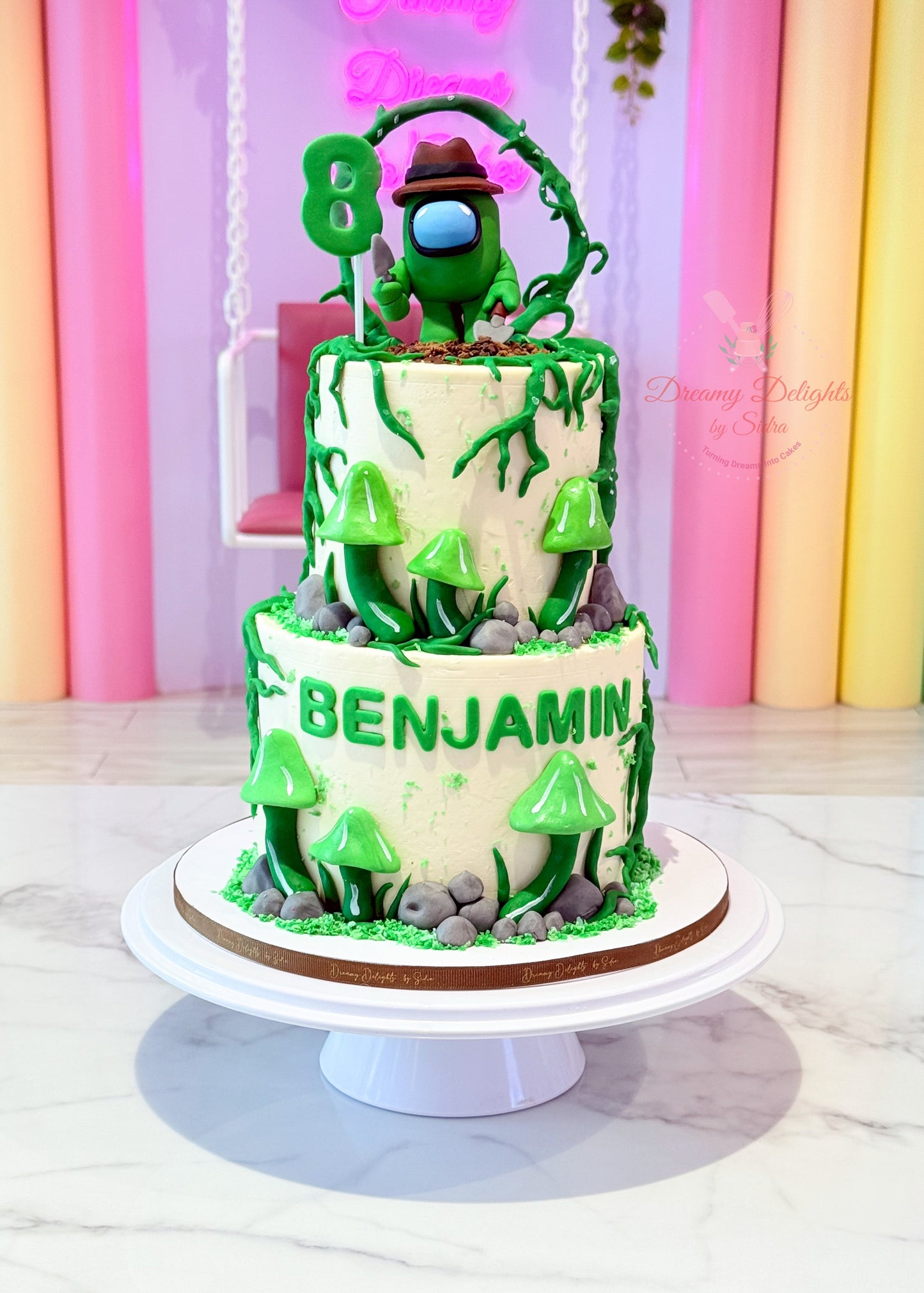 Two-tier birthday cake with green camouflage design and 'Benjamin' on a white stand.