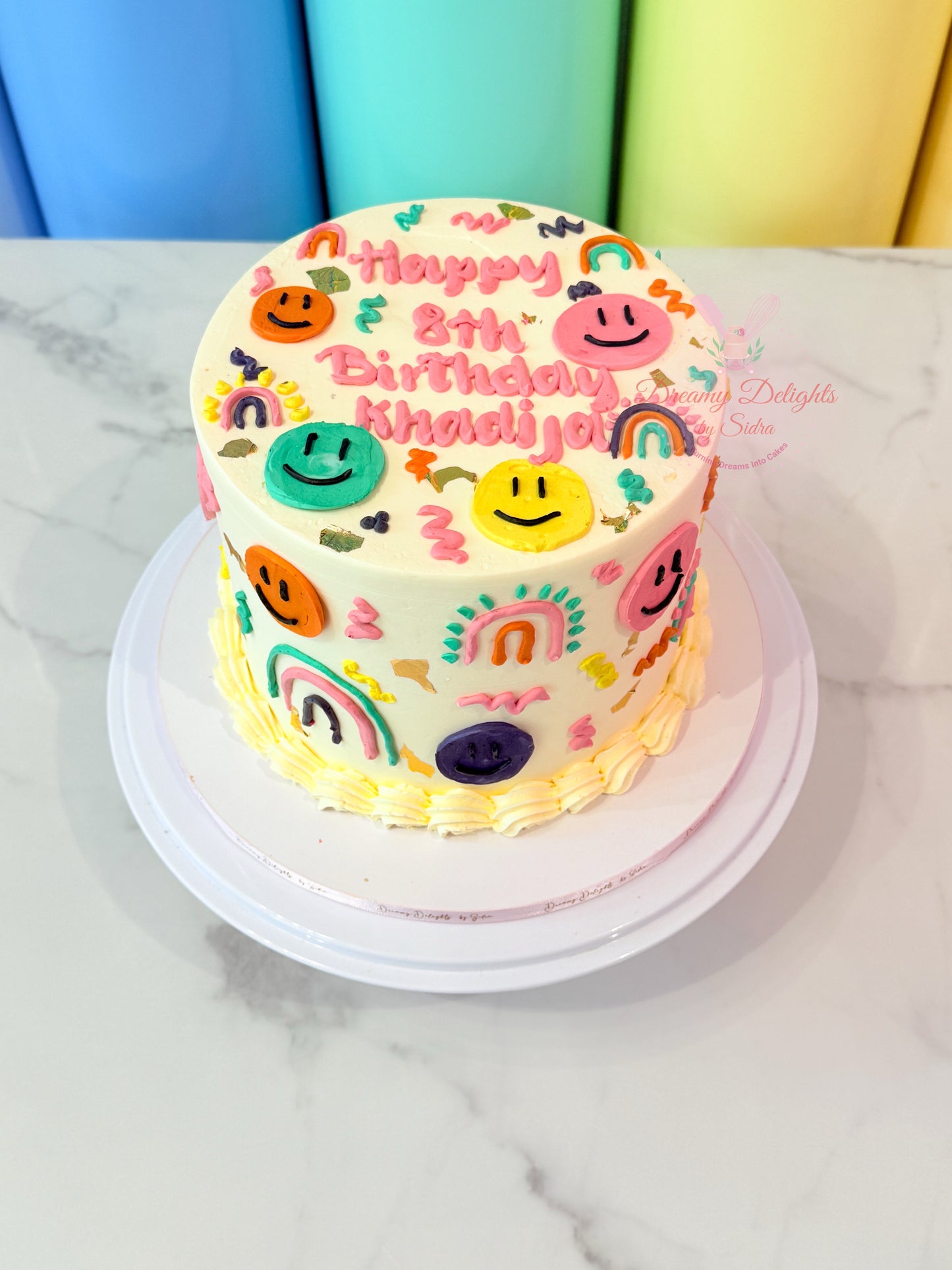 Colorful birthday cake with smiley faces and rainbow decorations on a white marble surface.