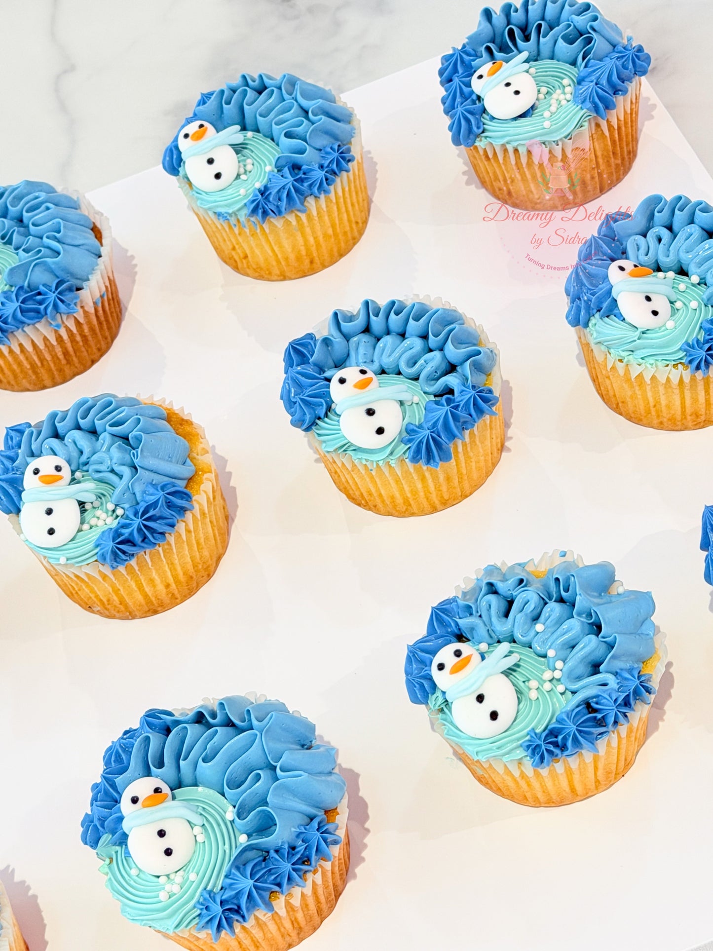 Cupcakes decorated with blue frosting and snowman decorations on a white surface.