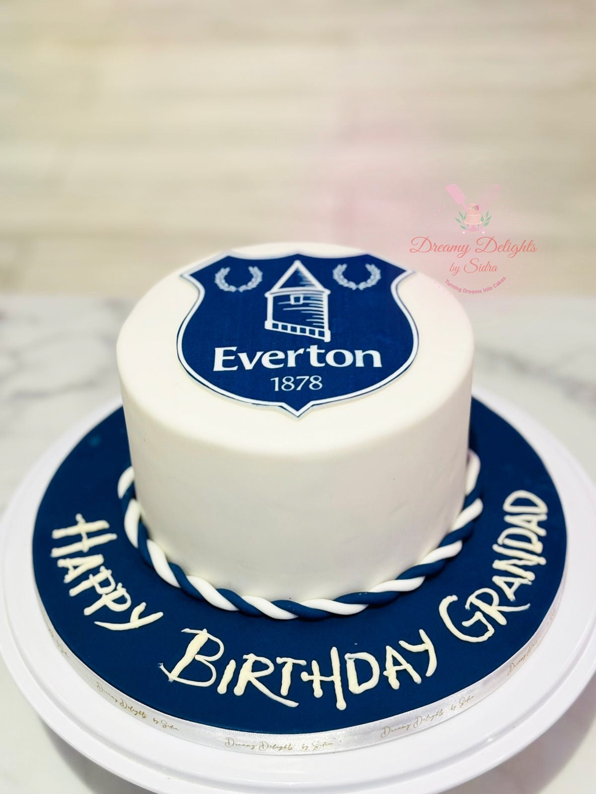 White cake with Everton logo and 'Happy Birthday Grandad' text on a blue cake board.