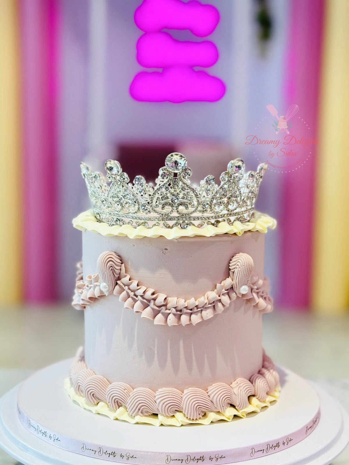 Pink cake with a silver crown decoration against a colorful background