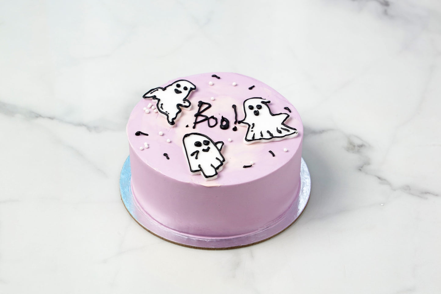 Pink cake with ghost and 'Boo' decorations on a marble surface