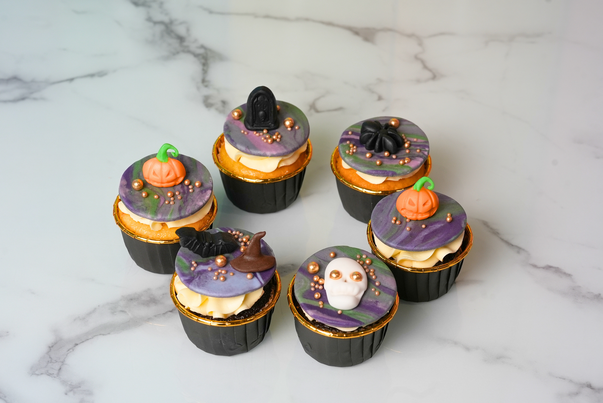 Six Halloween cupcakes decorated with pumpkins, skulls, bats, spiders, and purple icing by Dreamy Delights by Sidra in Dubai.