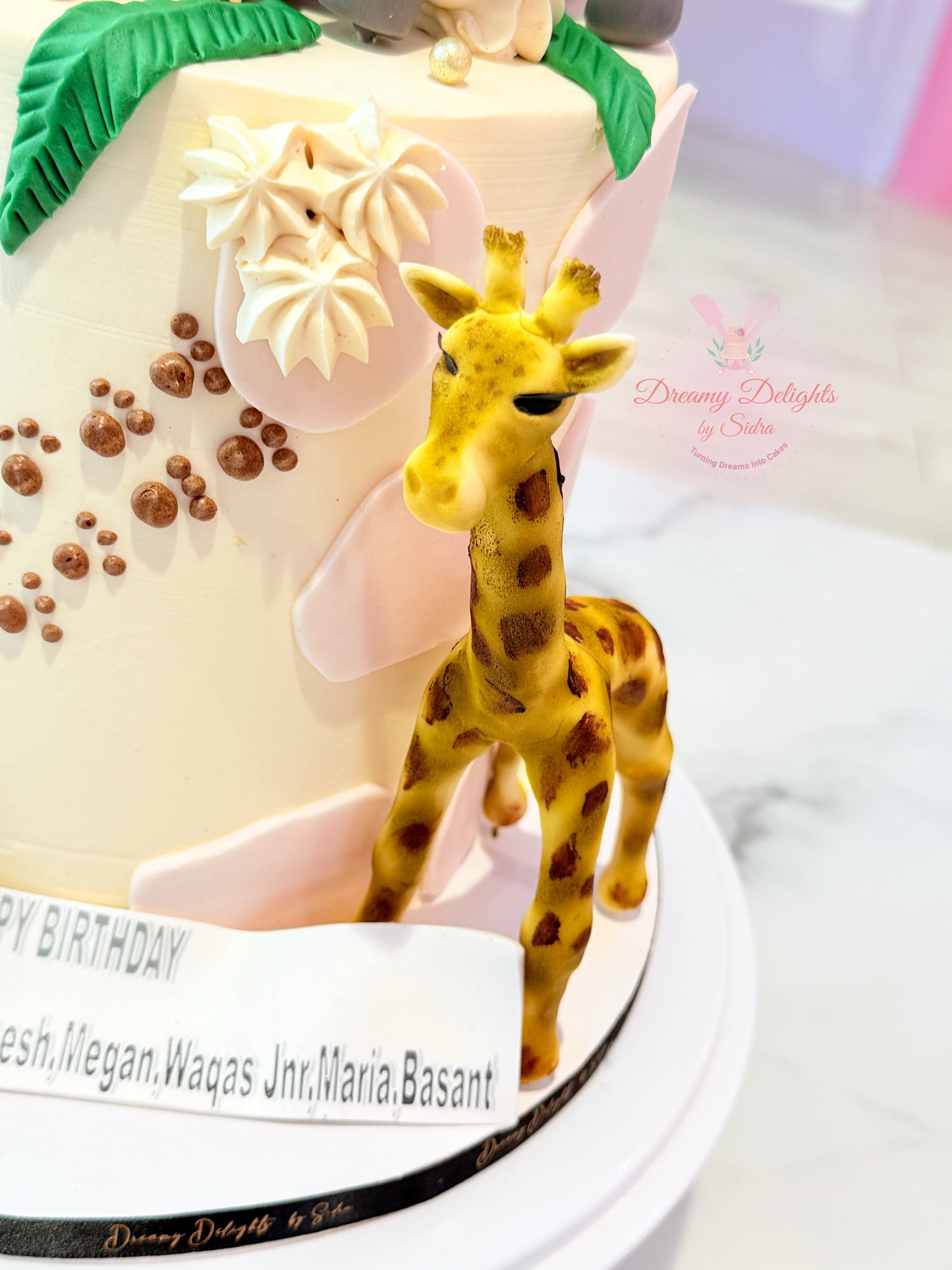 Birthday cake with a giraffe figurine on top, featuring decorative elements and text.