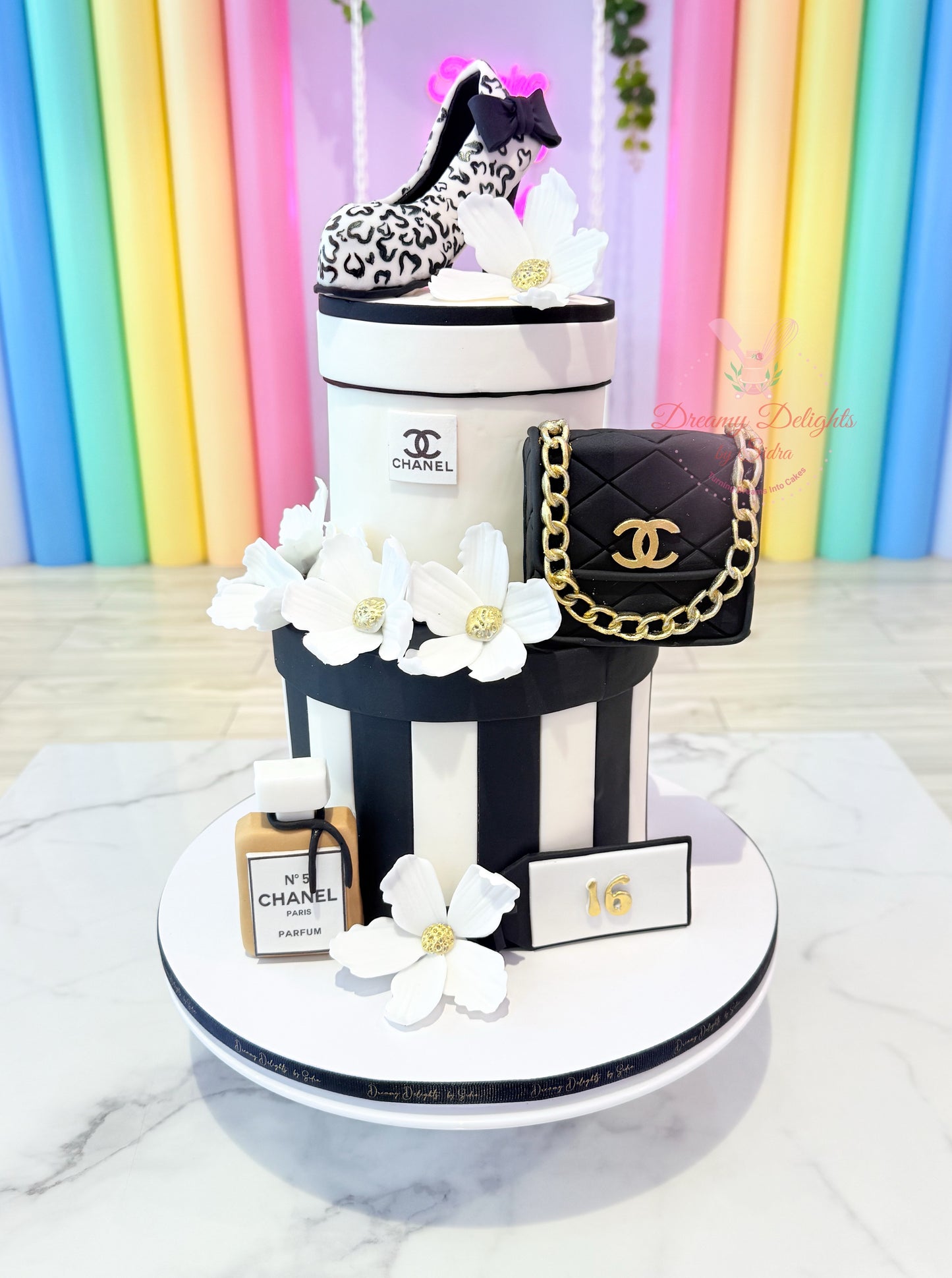 Chanel-themed cake with black handbag, flowers, and bottle against a colorful background