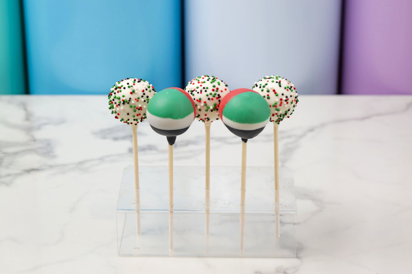 Colorful cake pops on sticks displayed on a marble surface with a colorful background