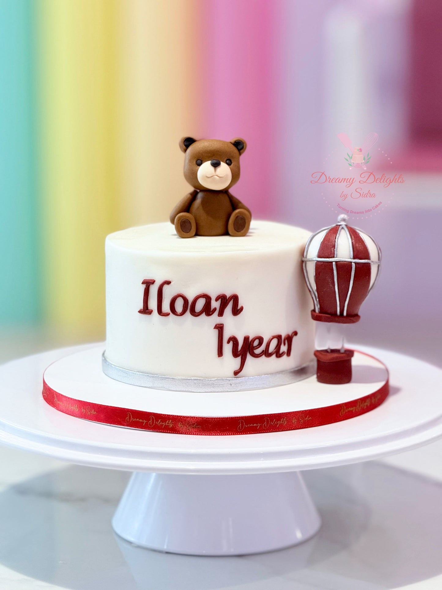 Birthday cake with teddy bear and hot air balloon decoration on a colorful background