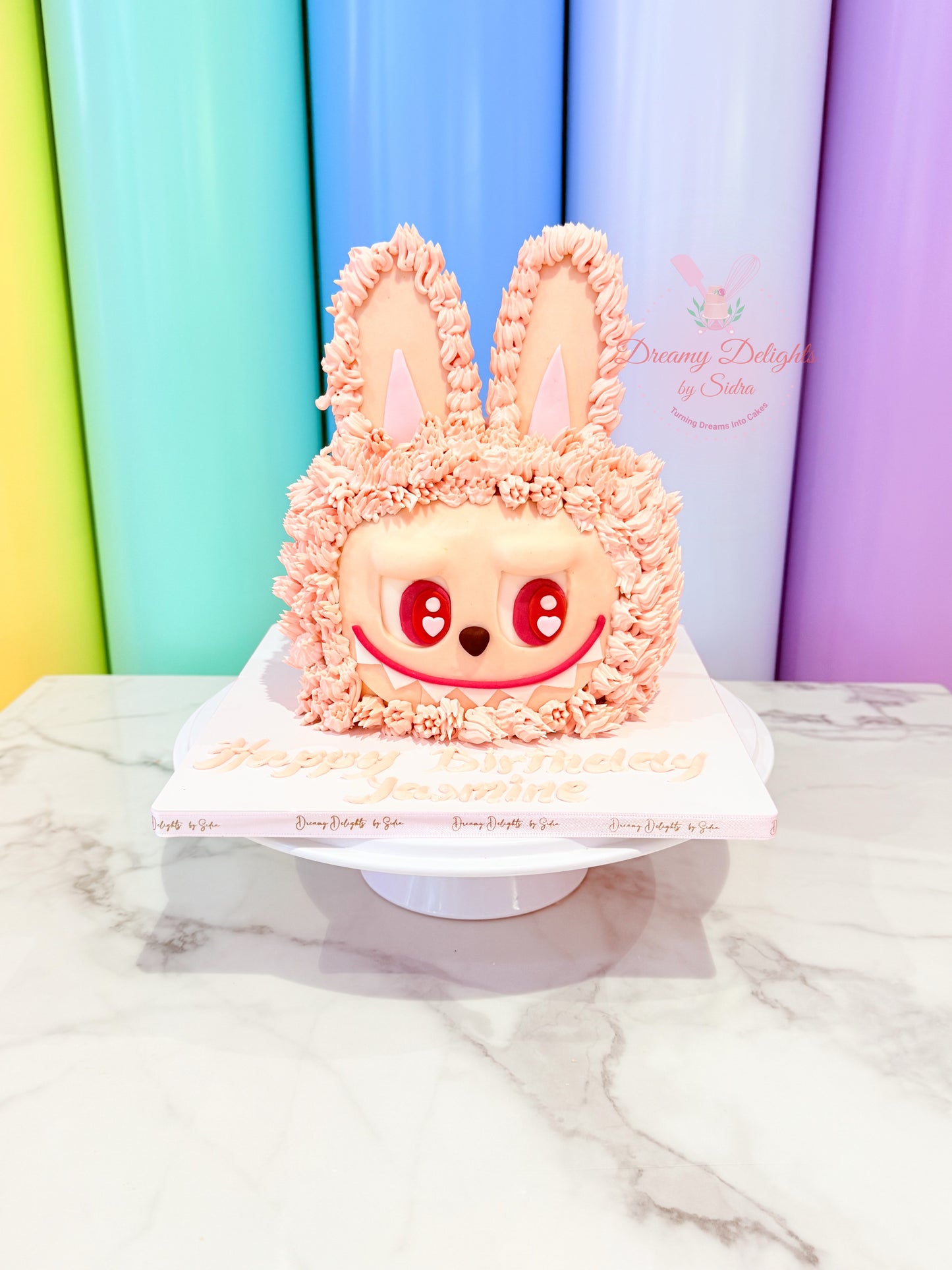 Pink rabbit-shaped cake with decorative ears on a white marble surface against a colorful background.