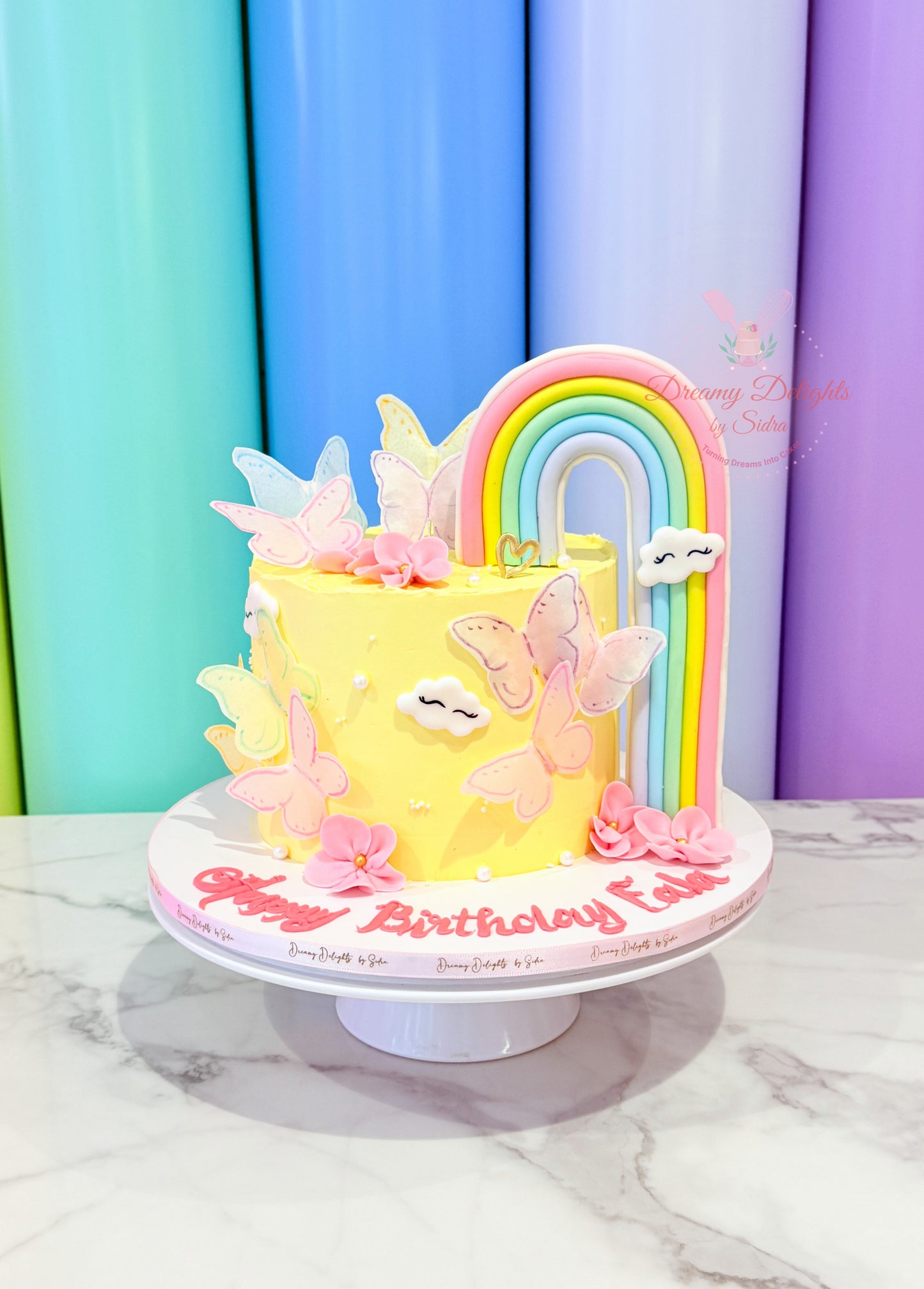 Colorful birthday cake with rainbow and butterflies on a marble surface.