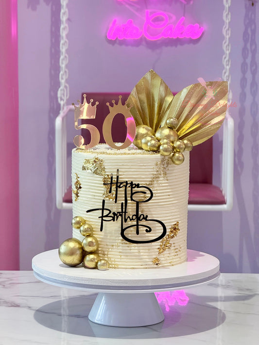 Decorative birthday cake with gold accents and 'Happy Birthday' text on a white stand.
