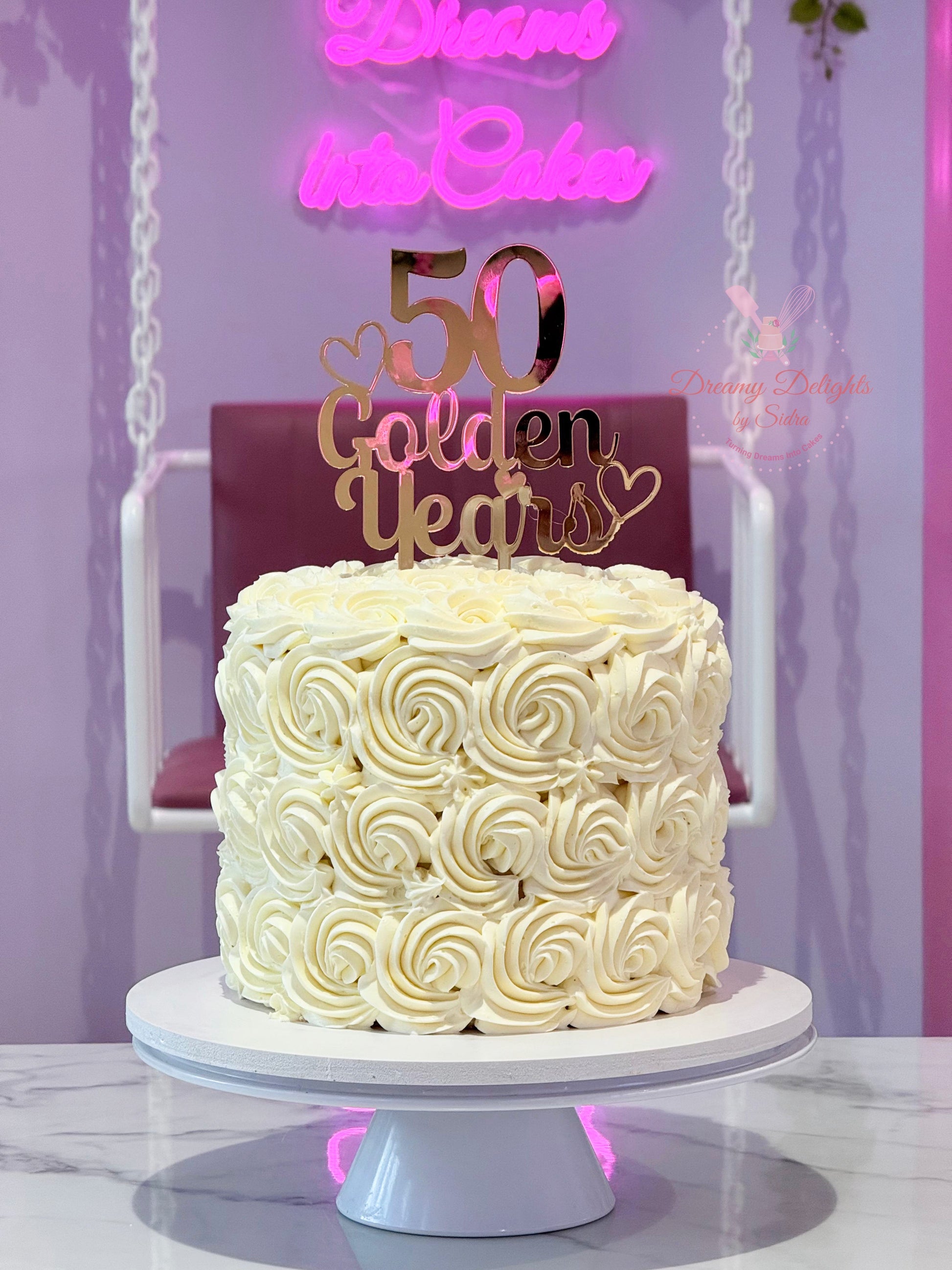 White cake with '50 Golden Years' topper on a stand against a purple background
