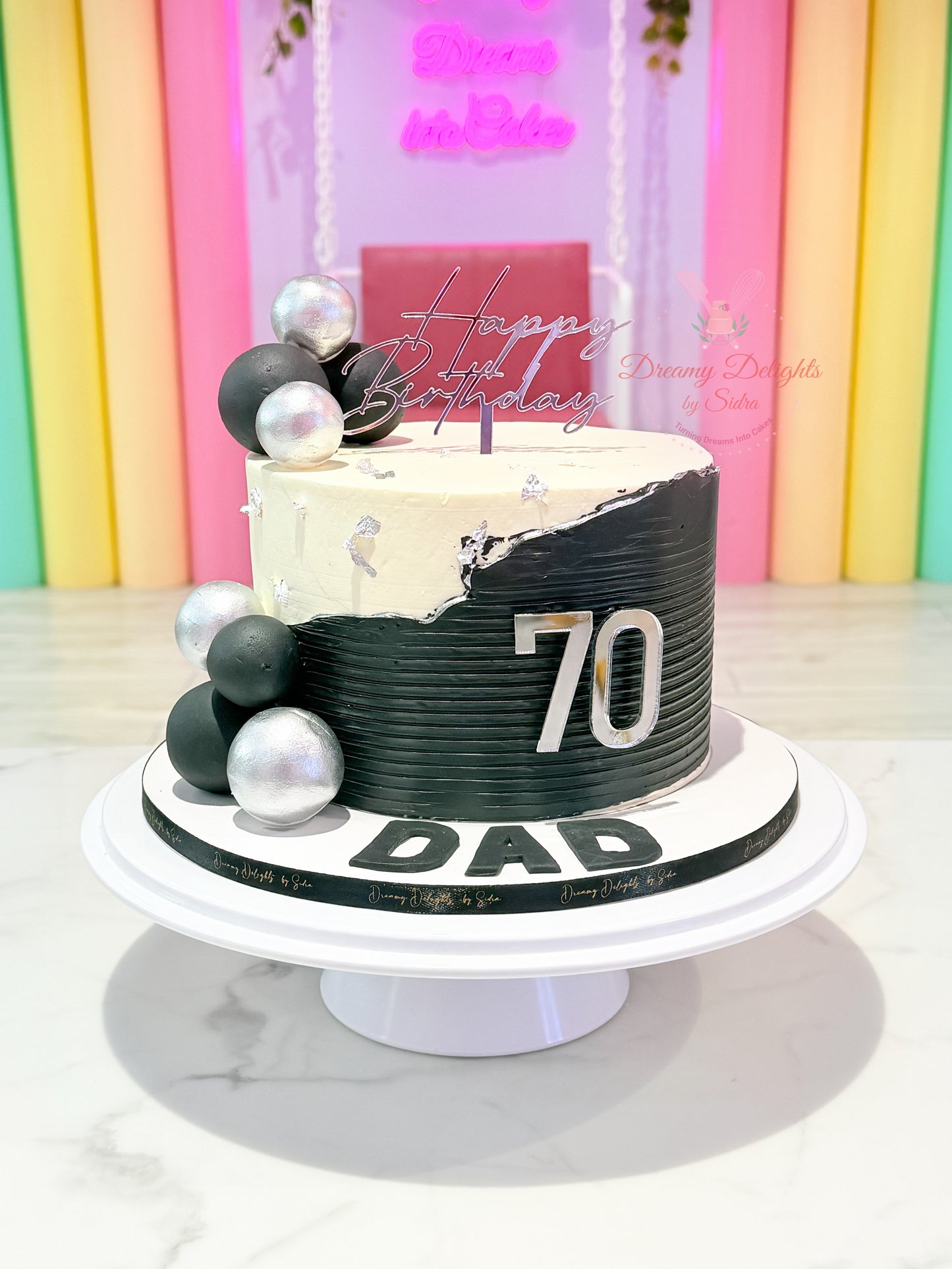 70th birthday cake for dad with black and white buttercream finish, silver decorative accents, acrylic topper, and custom age badge by Dreamy Delights by Sidra in Dubai.