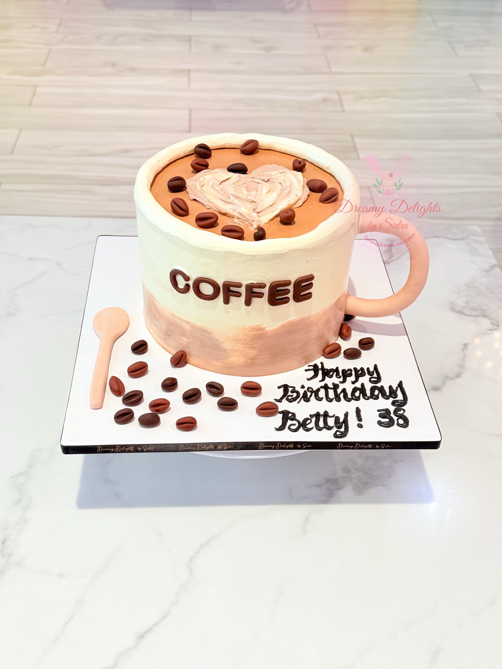 Birthday cake shaped like a coffee cup with coffee beans and a spoon on a white surface.