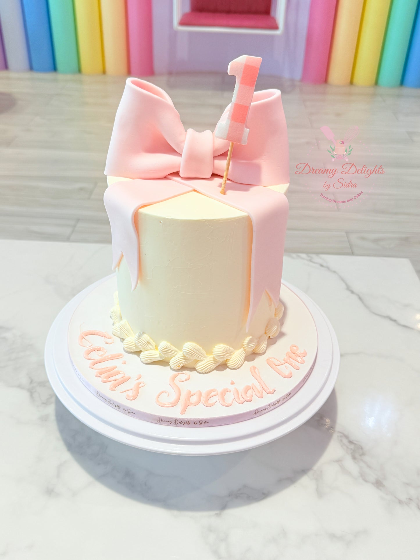 Pastel-colored cake with a pink bow and 'Lil's Special Day' text on a marble surface.