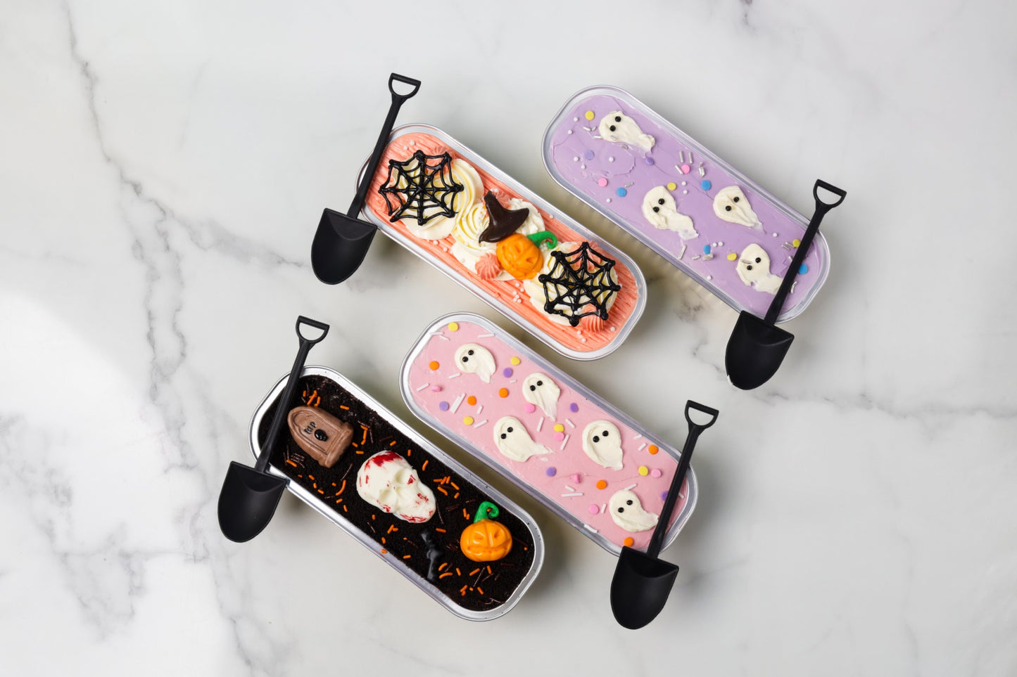 Four Halloween-themed dessert trays with decorative elements on a marble surface.