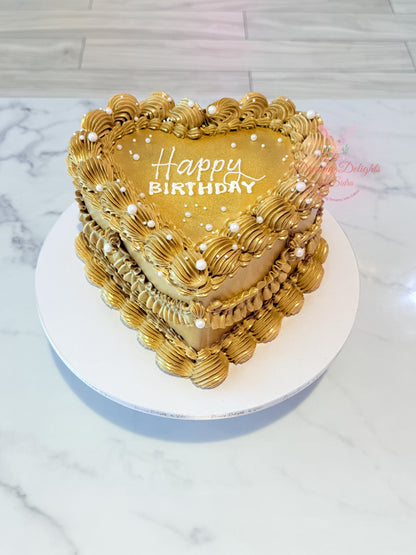 Heart-shaped birthday cake with gold icing and 'Happy Birthday' text on a marble surface.