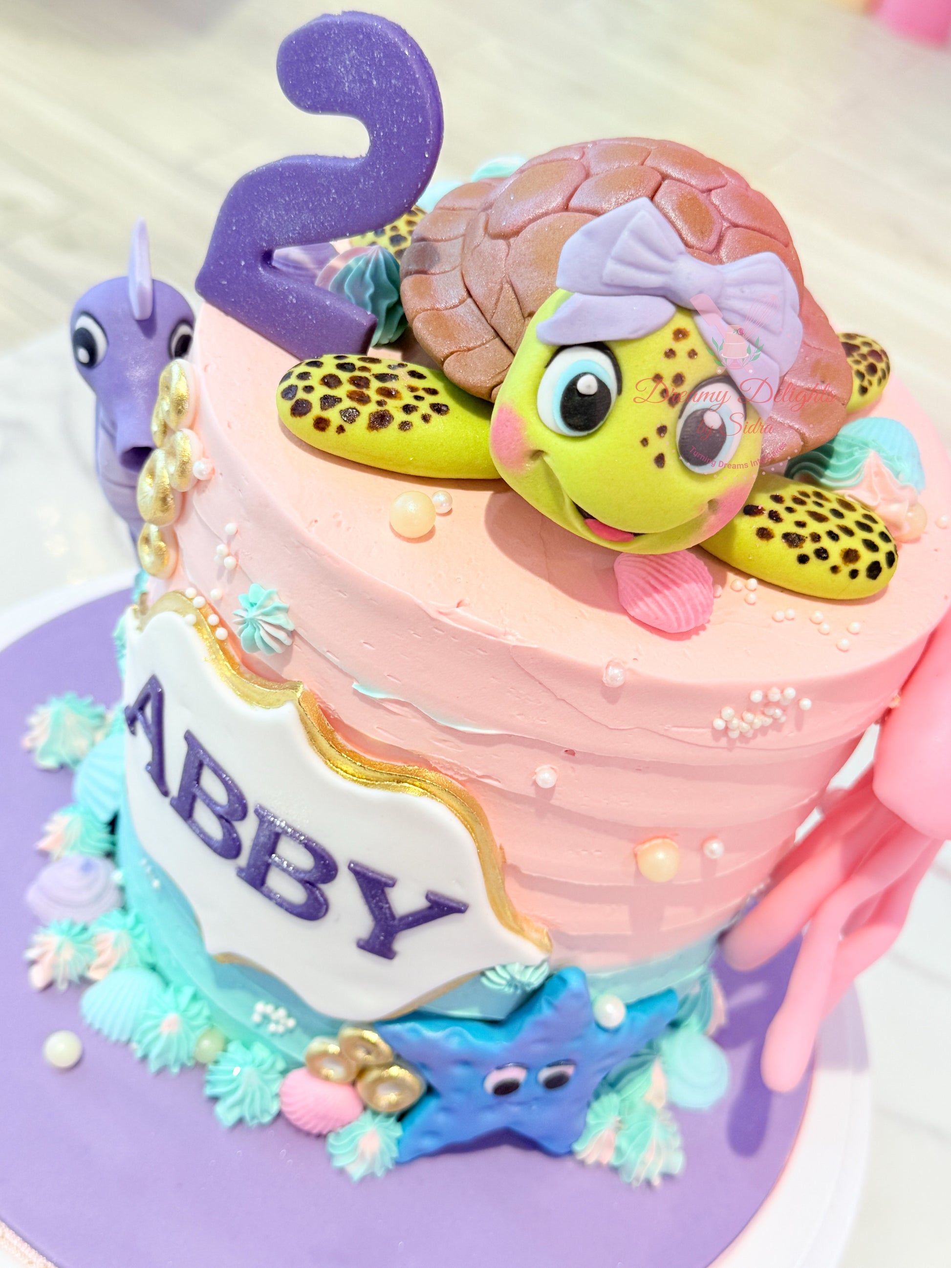 Birthday cake with a turtle character and the number 2, decorated with colorful icing and starfish.