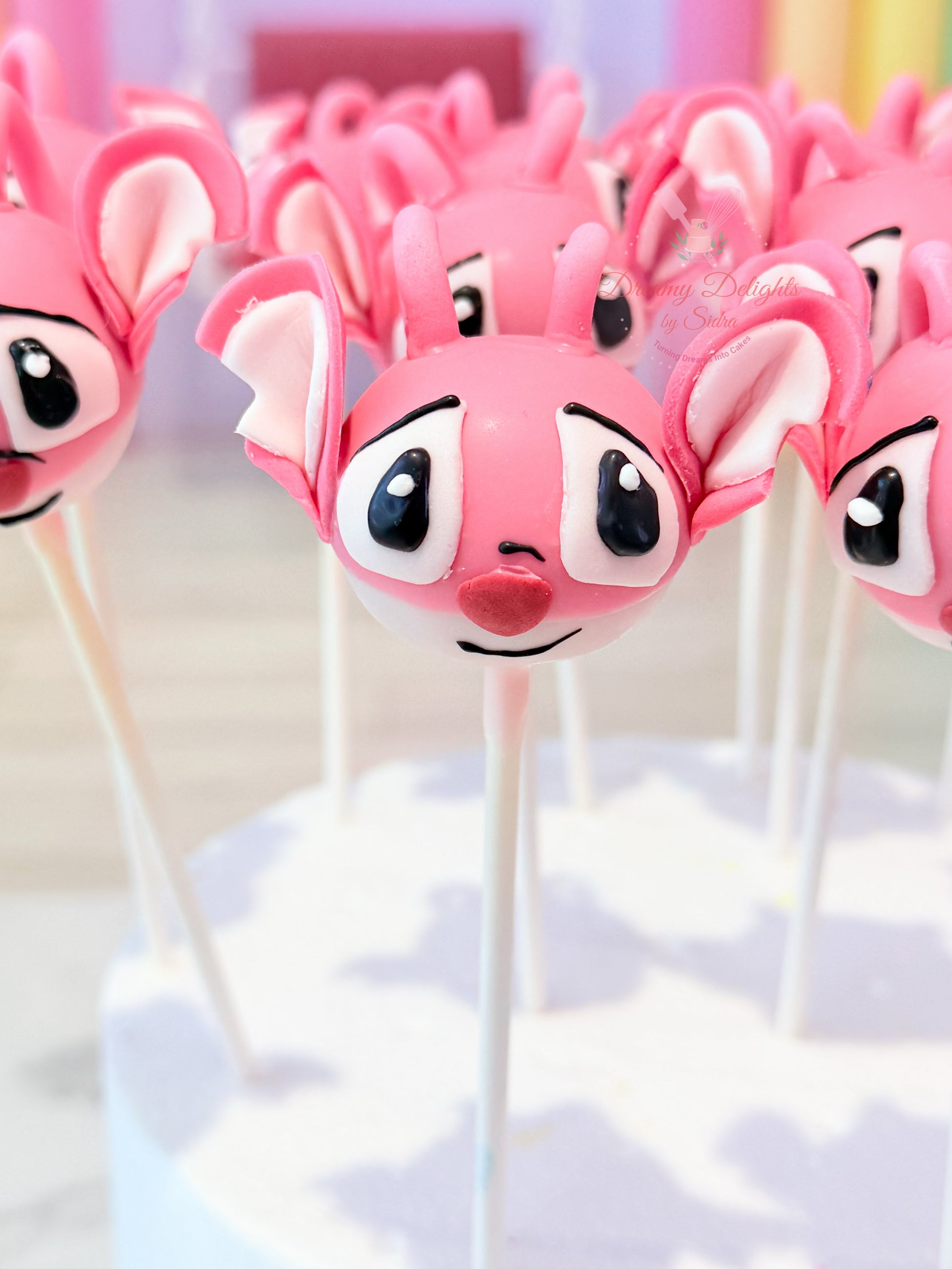 Pink character cake pops on sticks with a blurred background