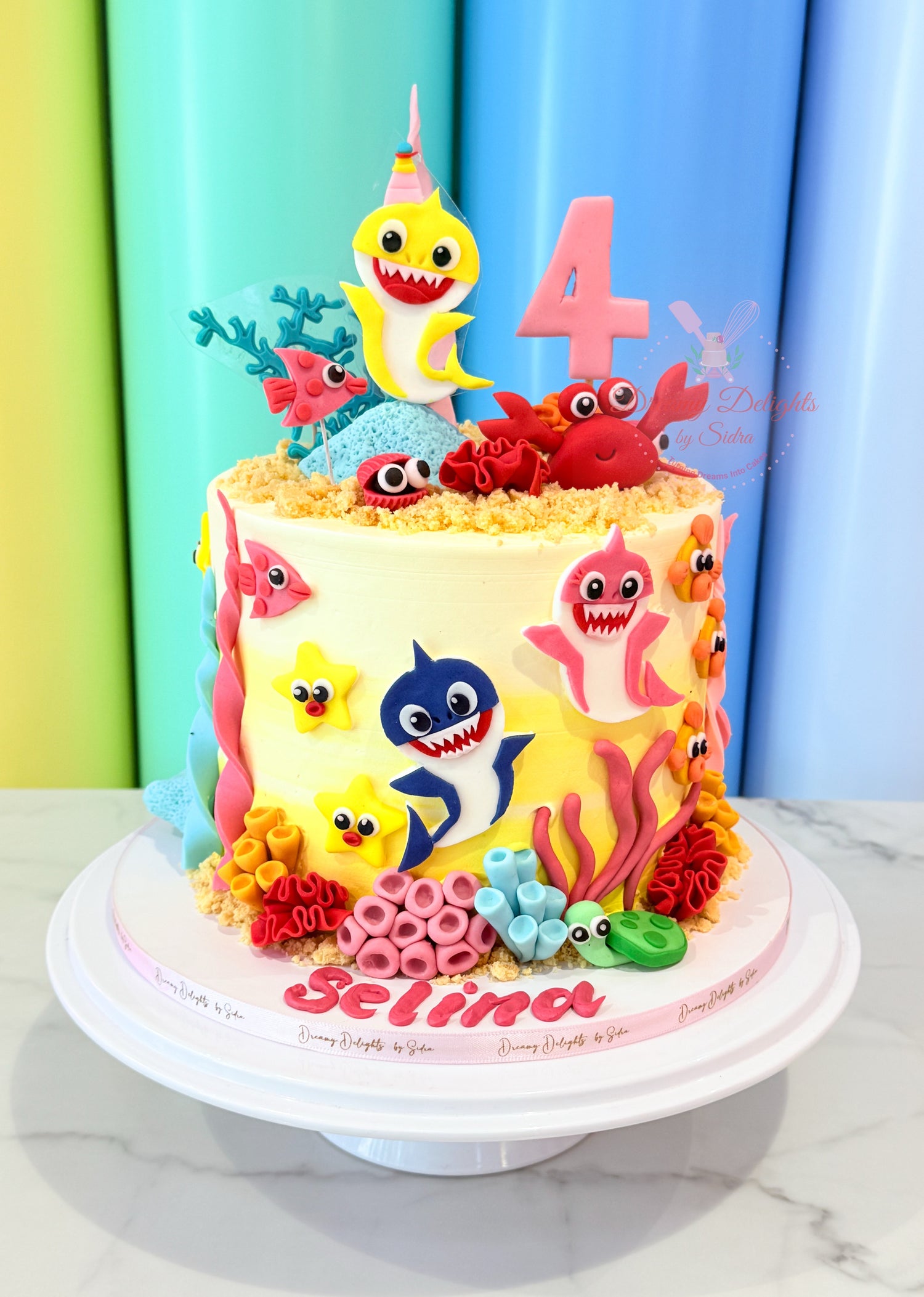 Colorful birthday cake with 'Baby Shark' theme and number 4 candle against a colorful curtain background.