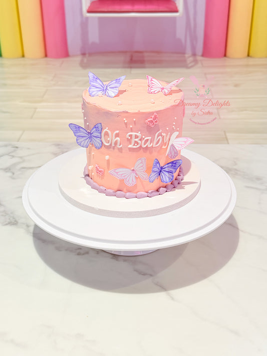 Oh Baby butterfly baby shower cake Dubai with pink frosting and delicate butterfly decorations by Dreamy Delights by Sidra
