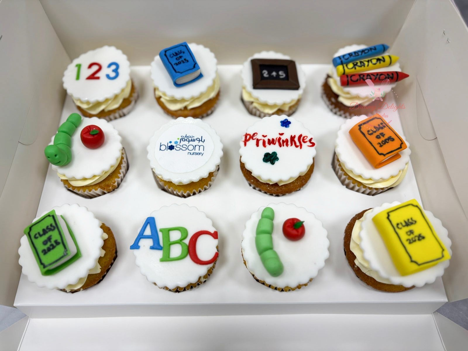 Box of cupcakes with educational-themed decorations including numbers, letters, and classroom items.