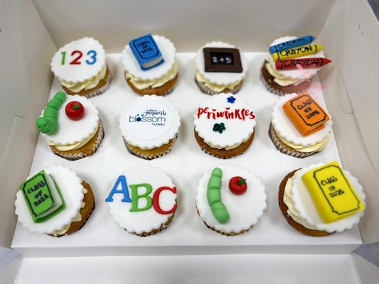 Box of cupcakes with educational-themed decorations including numbers, letters, and classroom items.