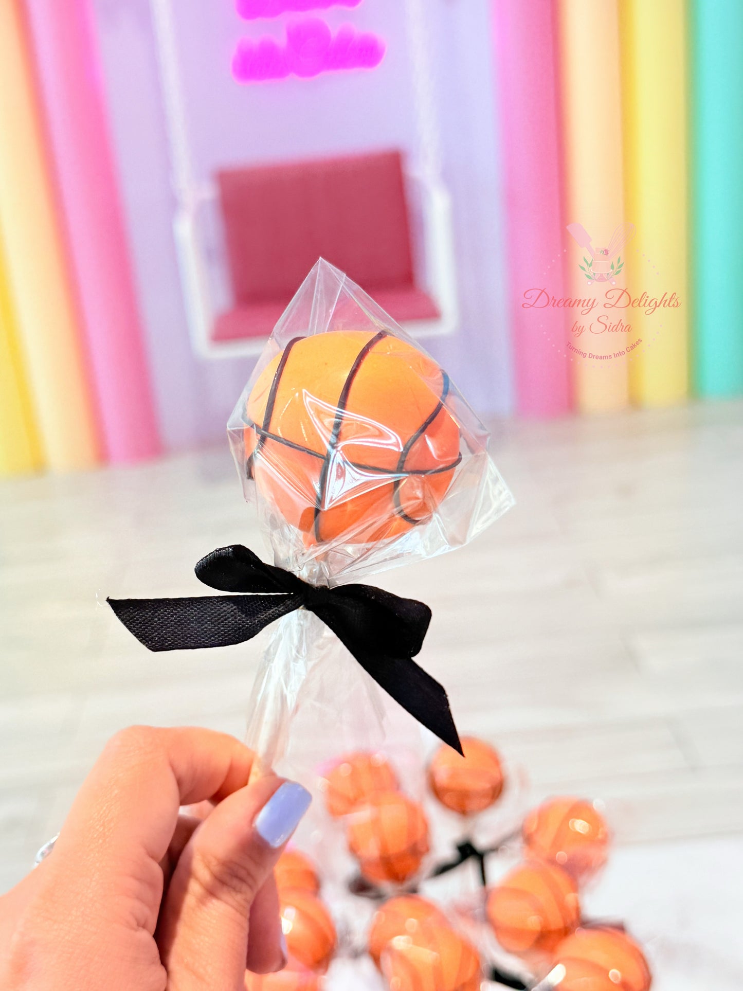 Basketball-shaped lollipop with a black bow in front of colorful curtains.