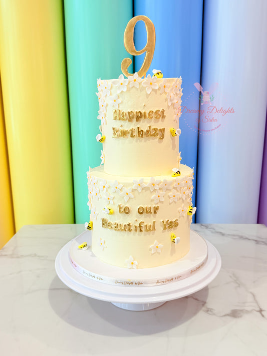 Two-tier birthday cake with gold decorations and a number 9 on a colorful curtain background