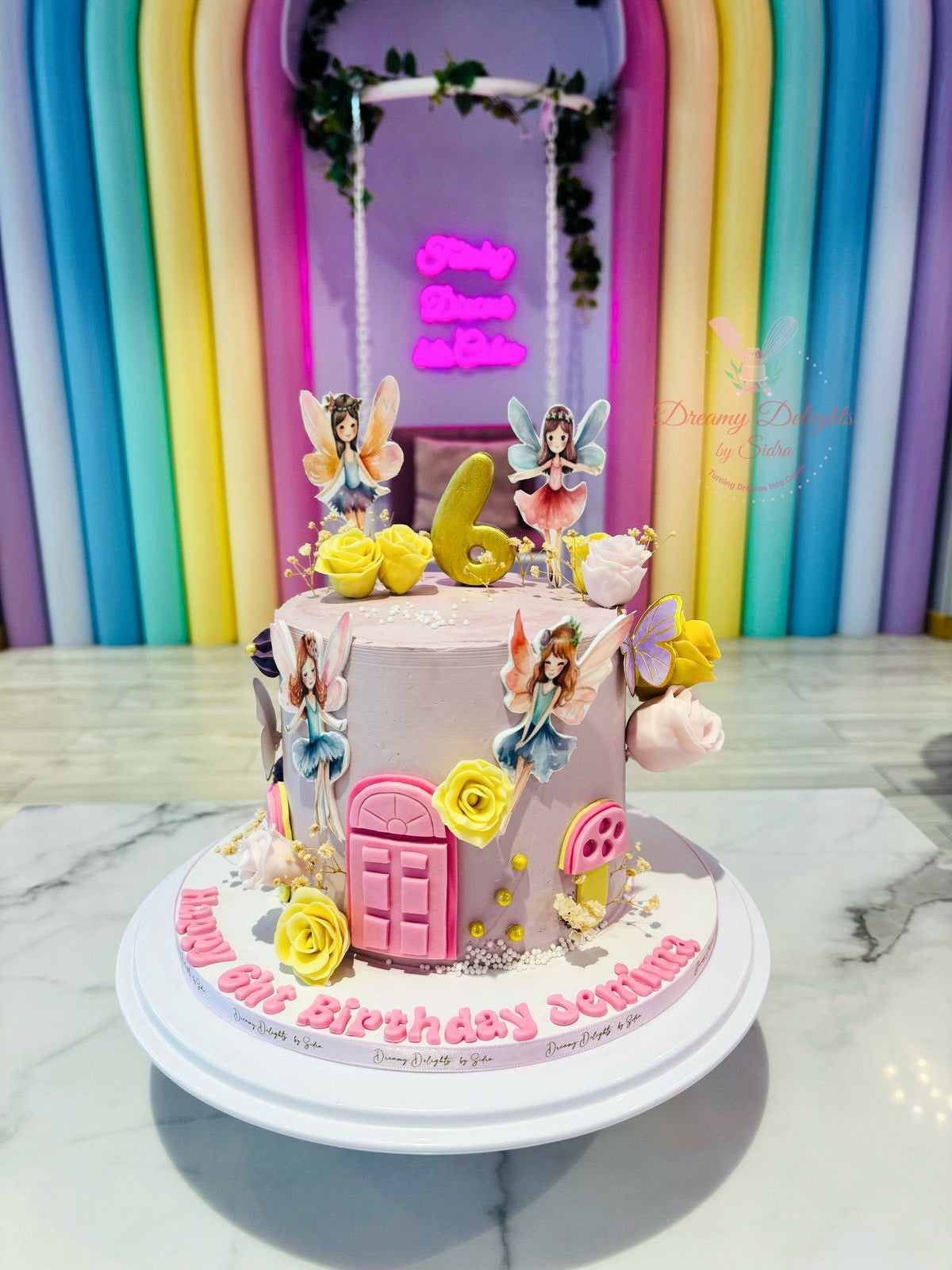 Children's birthday cake with fairies and a pink door design against a colorful curtain background.