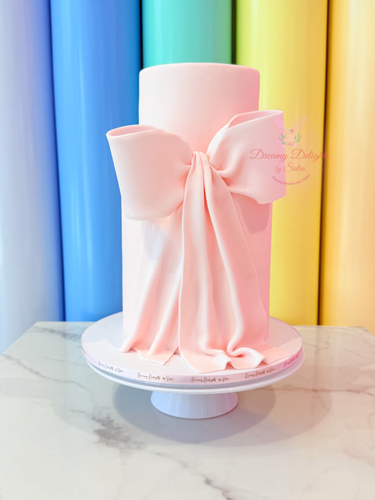 Pink cake with a large bow on a white stand against a colorful curtain background