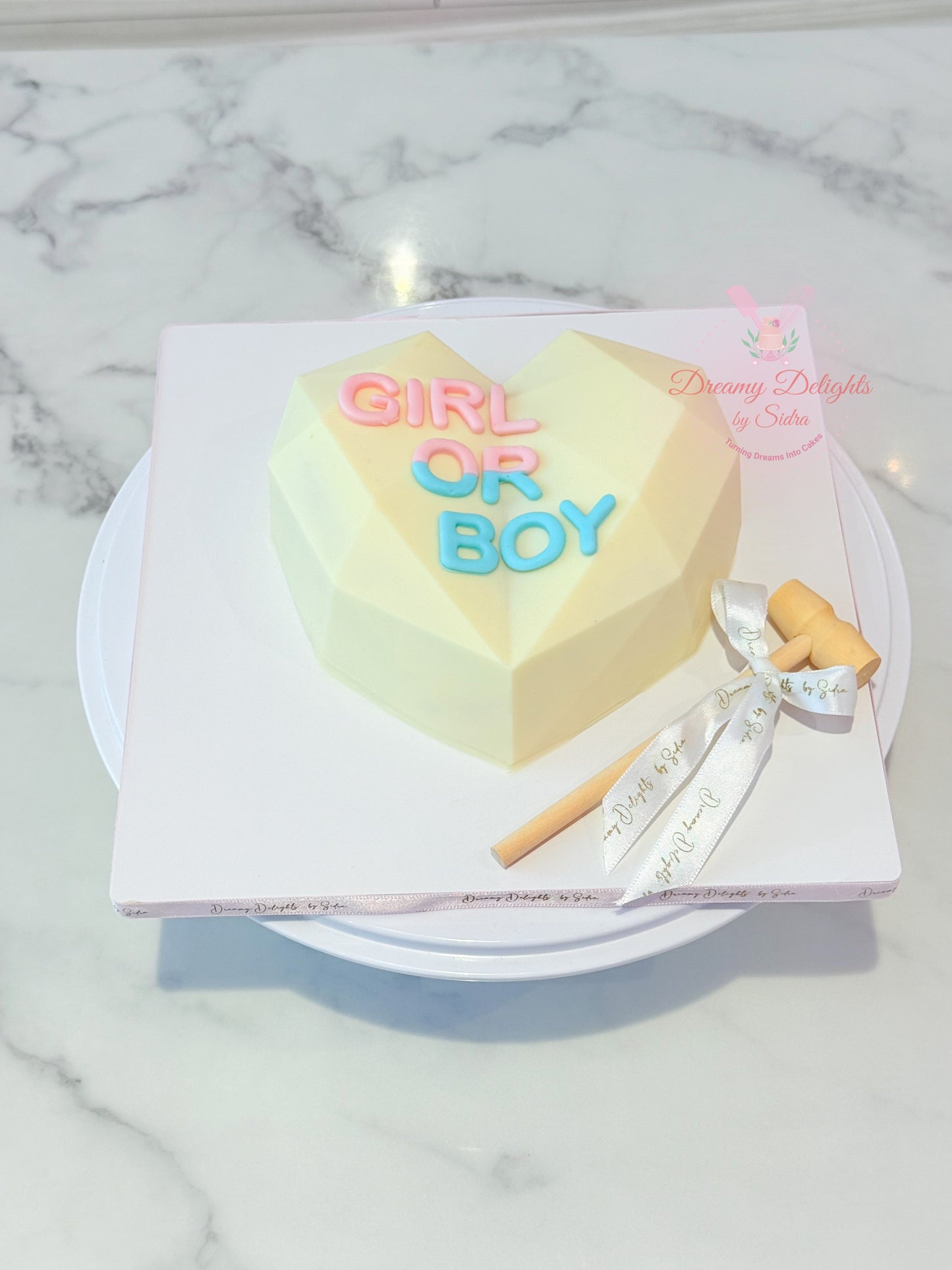 Heart-shaped cake with 'Girl or Boy' text on a marble surface