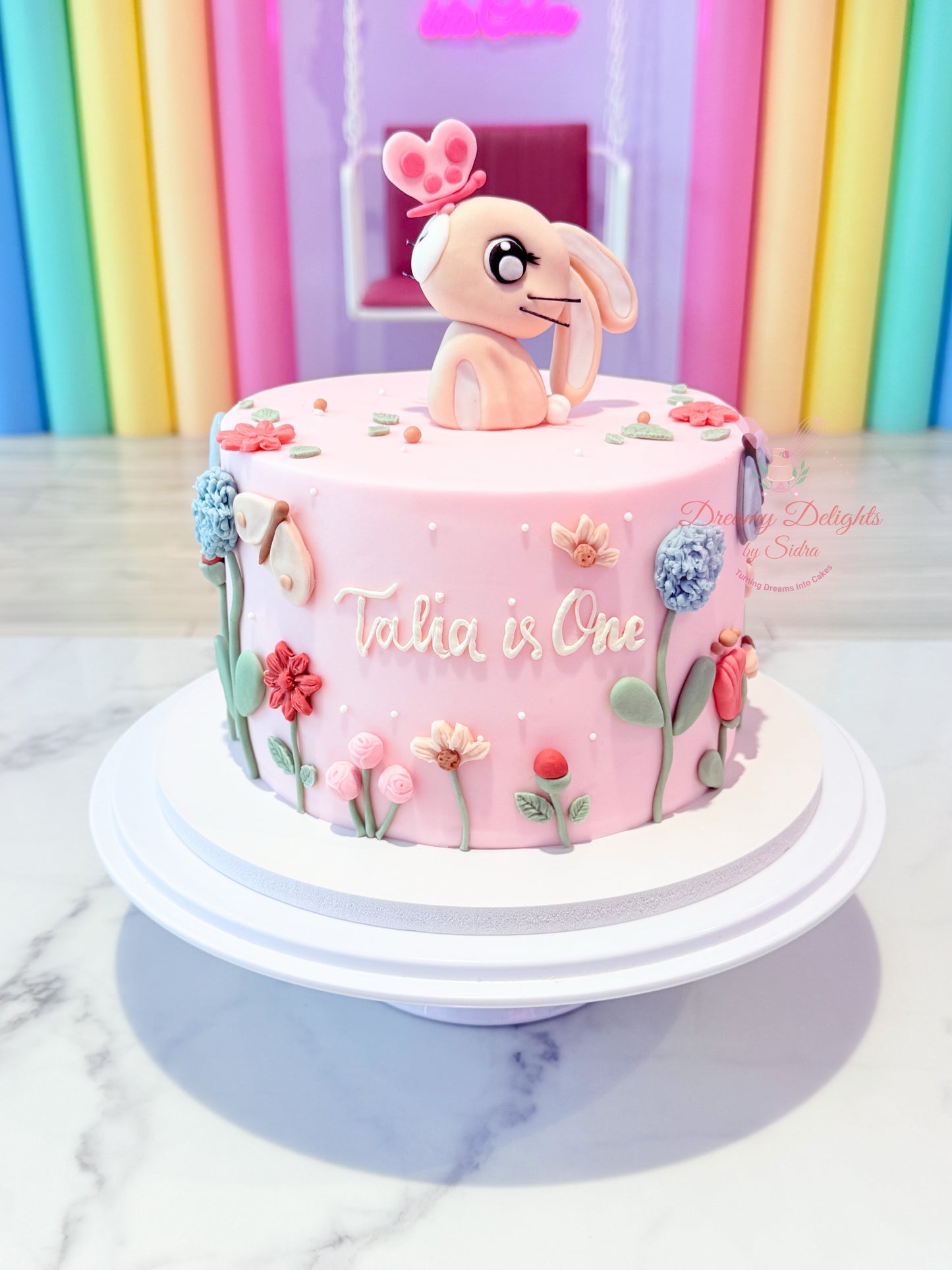 Bunny flowers first birthday cake for girls with pink floral theme and custom name in Dubai