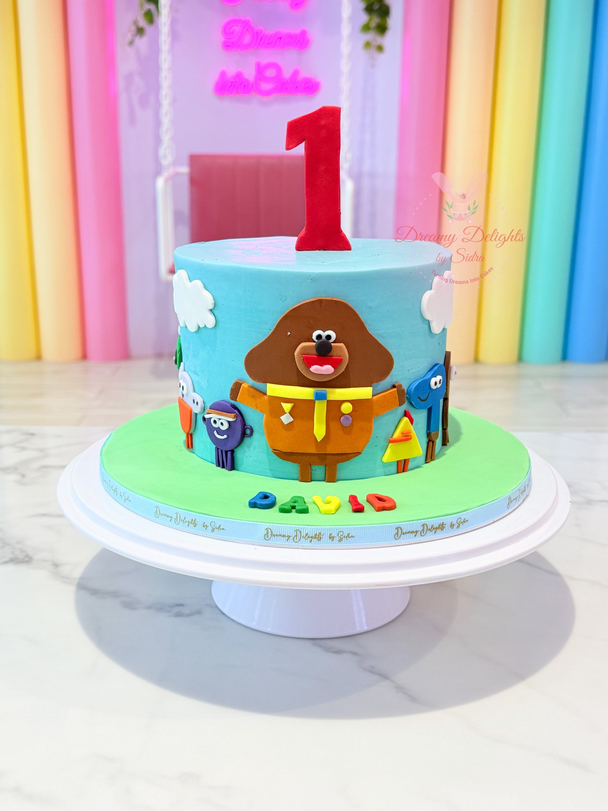 Duggee cake for boys Dubai with blue buttercream, colourful characters and a personalised age by Dreamy Delights by Sidra