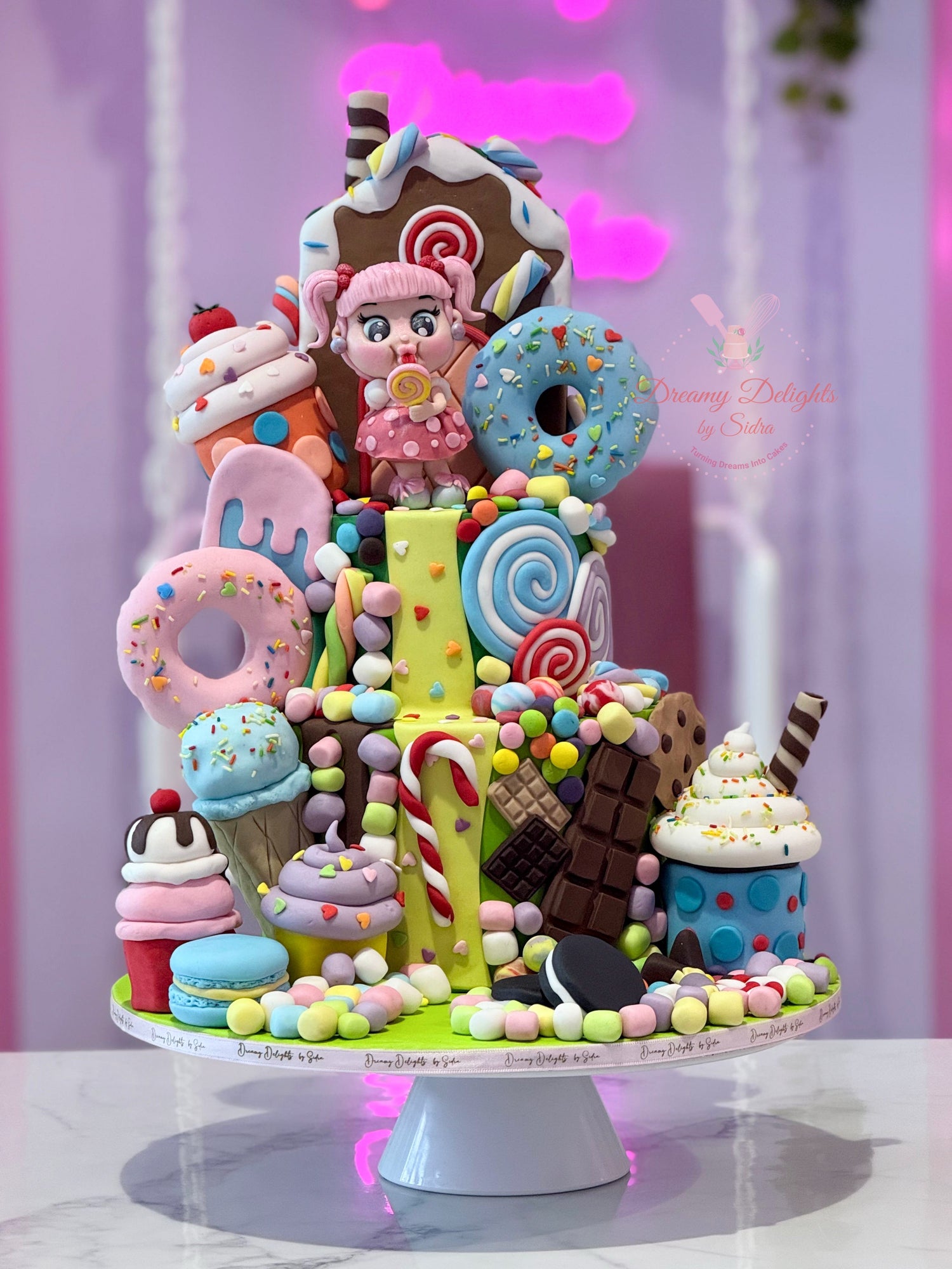 Colorful candy sculpture with a character figure on a white stand against a light purple curtain.