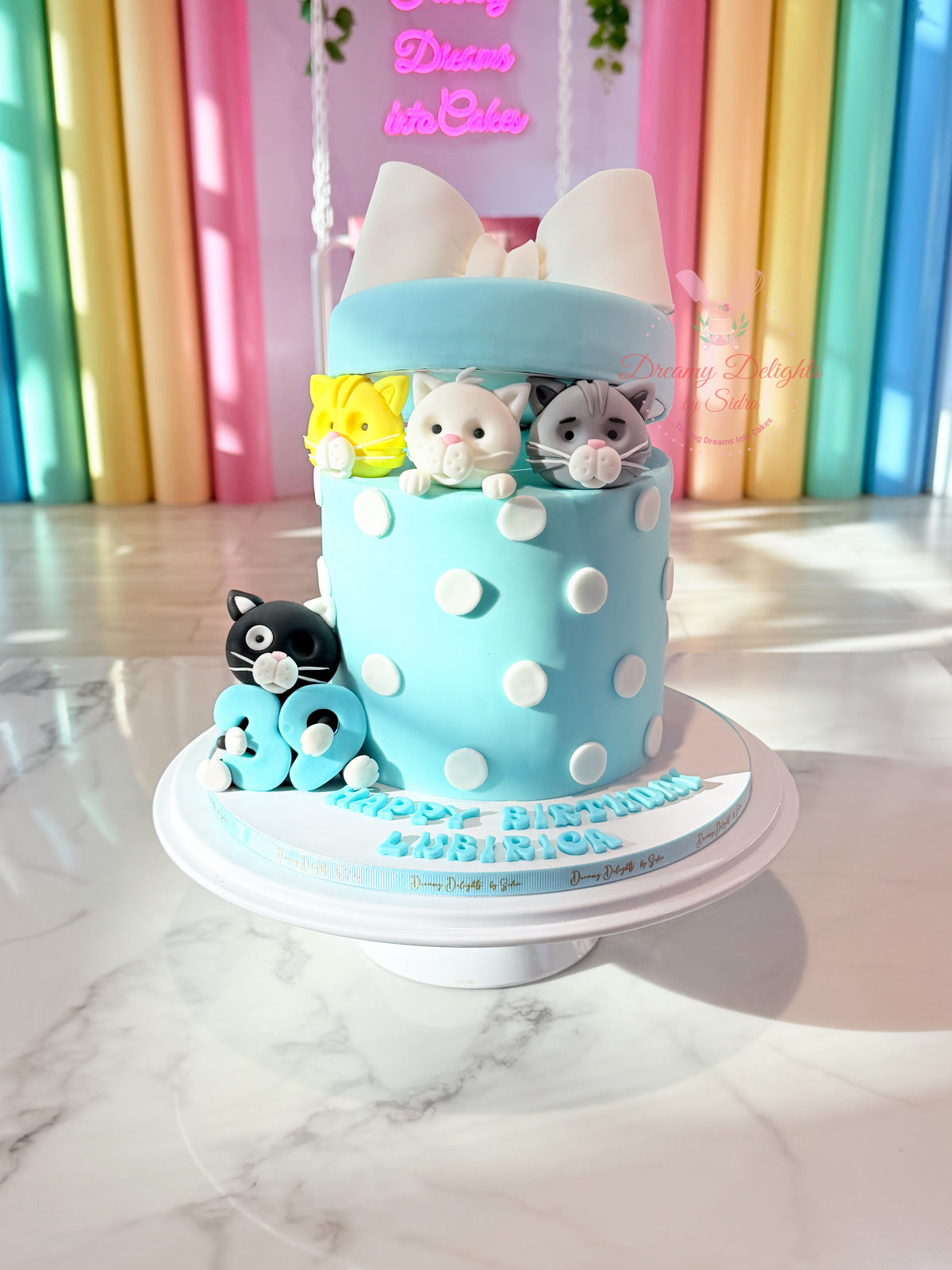 Cute cat gift box birthday cake Dubai with pastel blue frosting, white polka dots, large bow and adorable cat figurines by Dreamy Delights by Sidra.