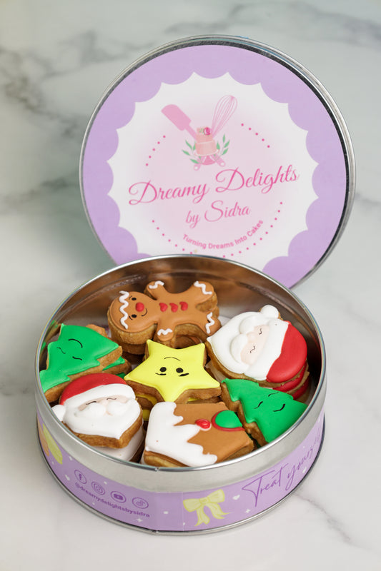Decorative cookie tin with colorful cookies shaped like gingerbread men, stars, and other shapes on a marble surface.