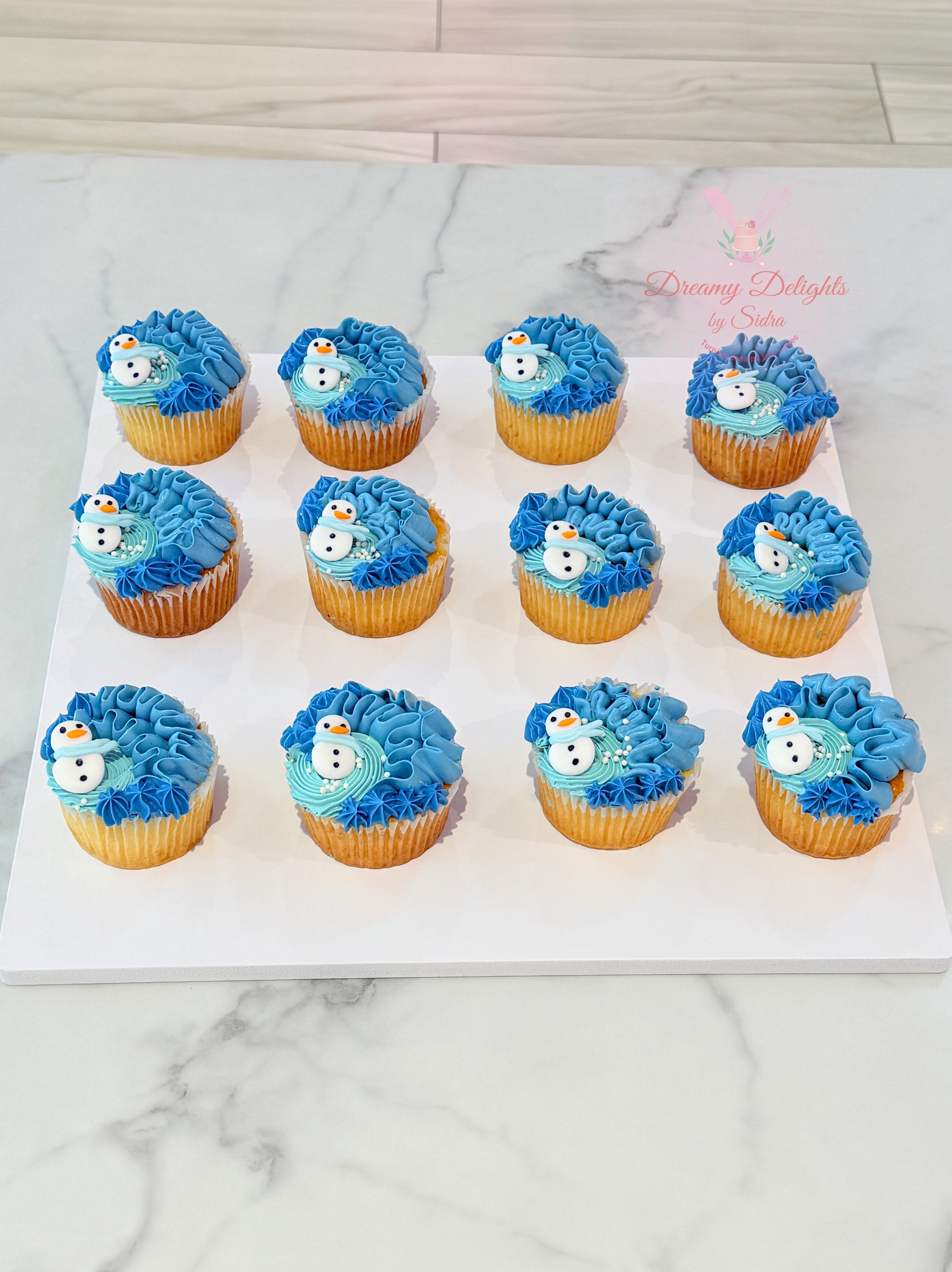 Row of blue-themed cupcakes on a white marble surface with 'Baking Delights' branding.