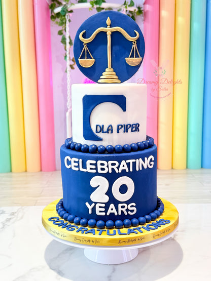 Corporate anniversary cake Dubai with blue tiers, gold scales and company branding by Dreamy Delights by Sidra.
