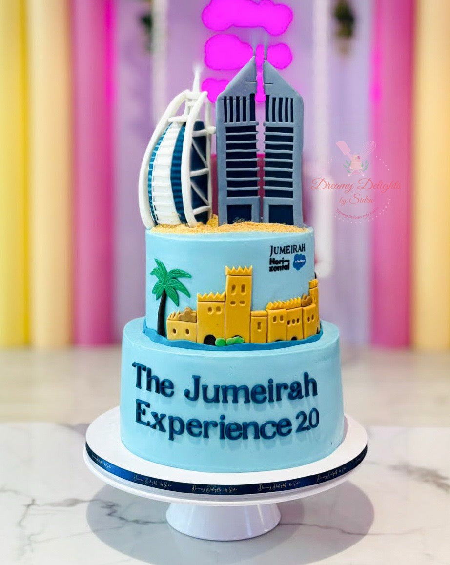 Two-tiered cake with Jumeirah Dubai logo and architectural elements on a colorful background
