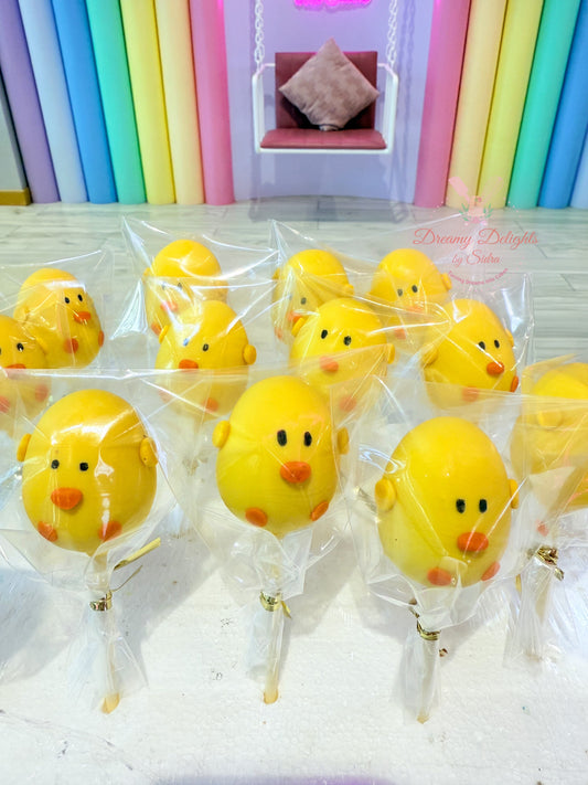 Yellow duck-shaped lollipops in clear packaging on a white surface with colorful background.
