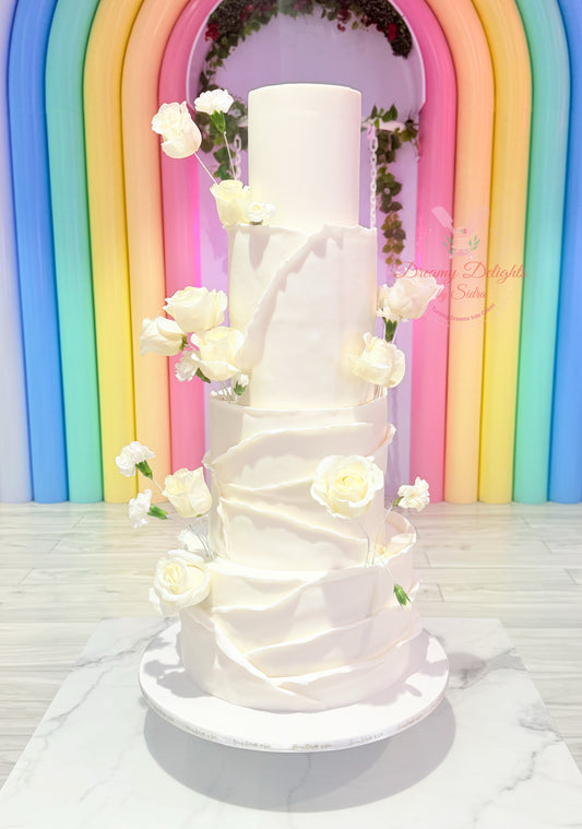 White wedding cake with floral decorations against a colorful arch background
