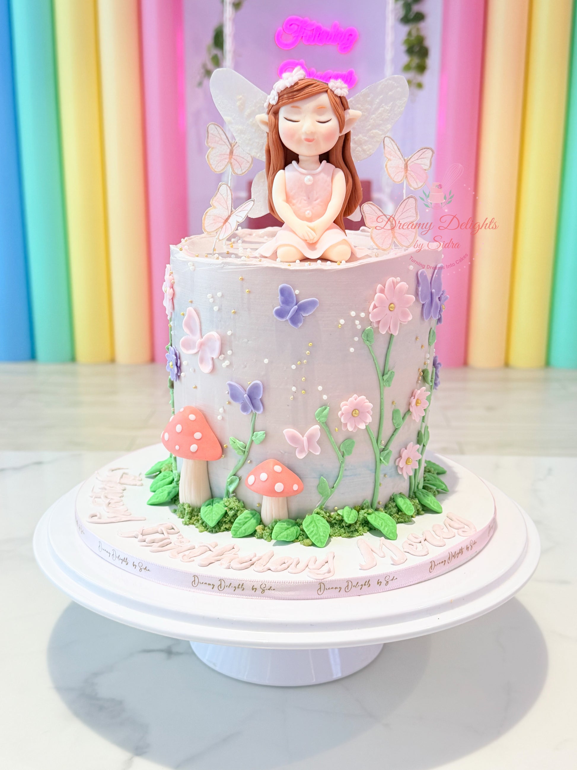 Pretty fairy garden cake for girls Dubai with fairy topper, butterflies, flowers and pastel garden decorations