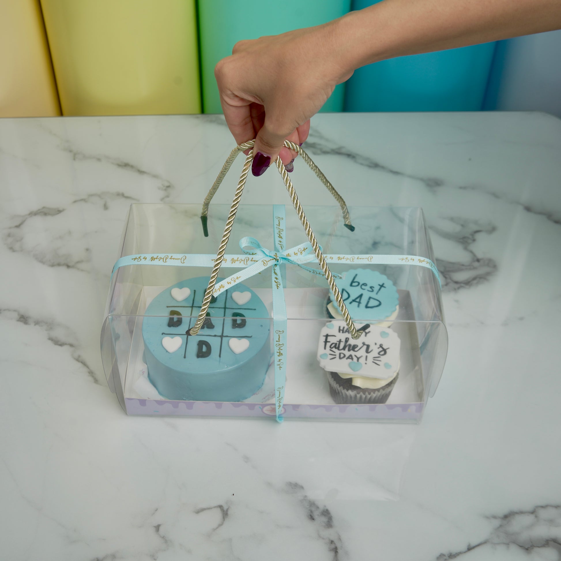Gift set with a blue item and a cupcake, tied with string, on a marble surface.