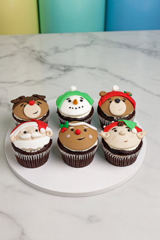 Six festive cupcakes with cartoon face designs on a marble surface.