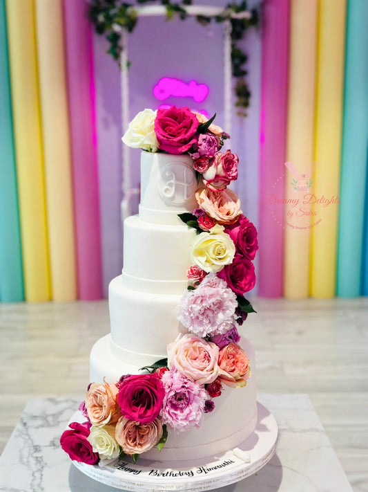 Multilayered cake decorated with colorful flowers against a vibrant, multicolored backdrop.