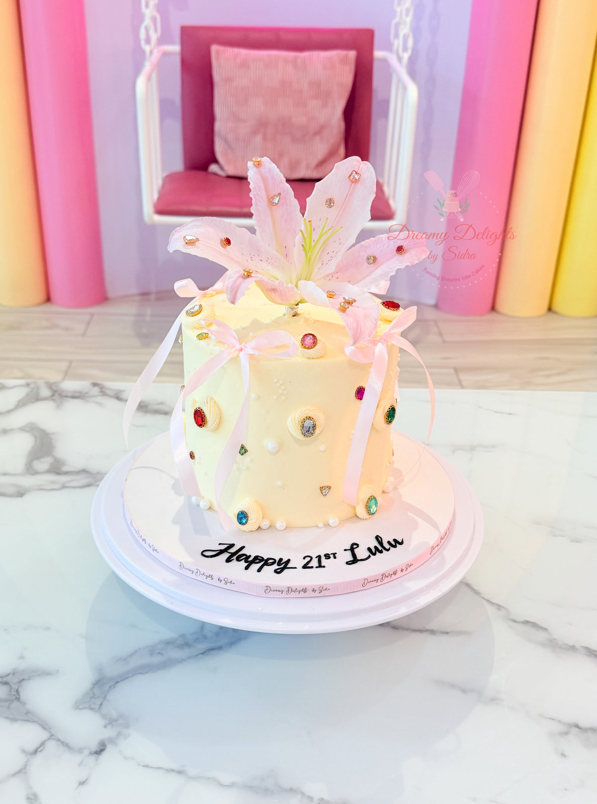 Gems Lily birthday cake with pink lily, colourful gems, pearls and ribbons by Dreamy Delights by Sidra in Dubai.