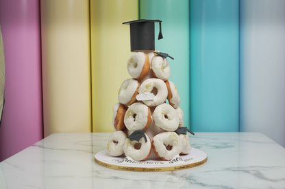 Graduation donut tower with white glazed donuts, graduation caps, and diploma decoration for graduation celebrations and parties.