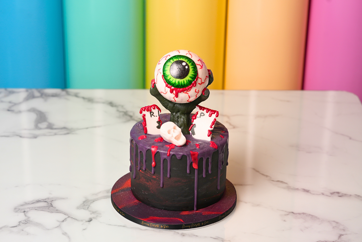 Halloween Big Eyeball Cake with dark frosting, purple drips, red details, and a giant eyeball topper by Dreamy Delights by Sidra in Dubai.